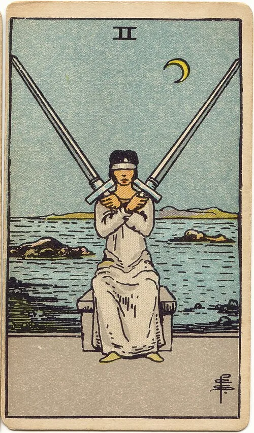 Mulher vendada de roupa clara sentada em banco, com braços cruzados e duas espadas erguidas, diante de mar rochoso e lua crescente à direita.